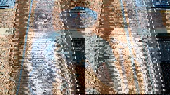 Mural of a man with a beard, sunglasses, and a guitar painted on a brick wall.