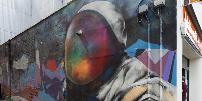 Colourful mural of an astronaut's helmet with a vibrant, abstract background on a brick wall.