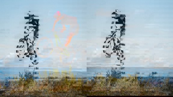 A cyclist mid-air performing a jump on the mountain bike trails at Cathkin Braes, with hills and sky in the background.