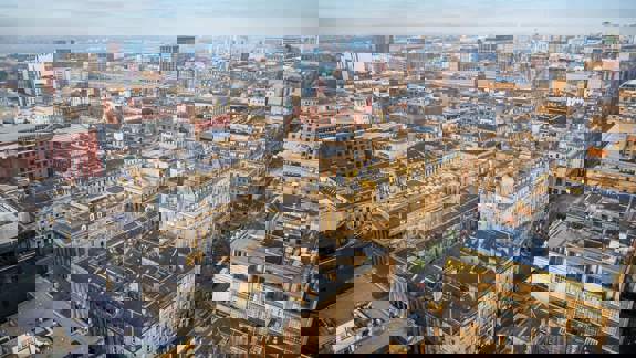 An aerial view of Glasgow city centre showing a dense grid system of buildings and streets under a bright sky, with a mix of old and modern architecture.
