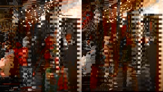 Groups of people chat and relax under fairy lights outside Sloans, a historic bar with a cosy atmosphere, during a lively evening.