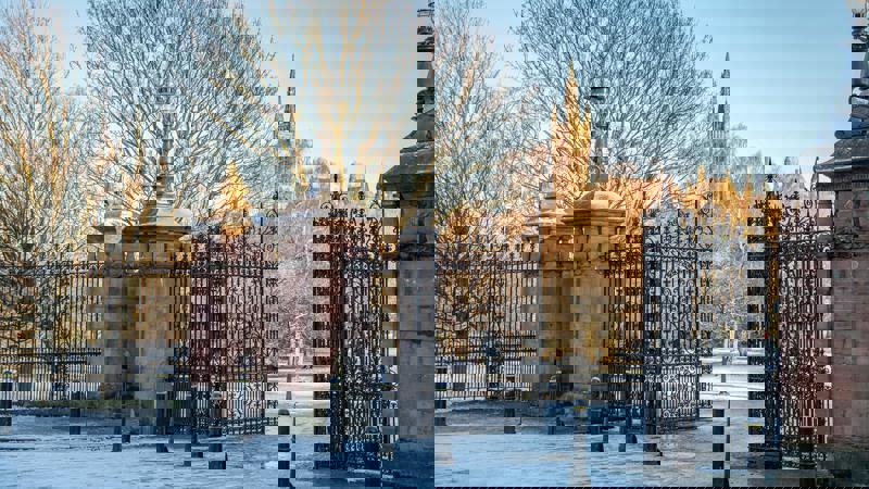 The grand entrance gates of Kelvingrove Park on a frosty winter day, with the University of Glasgow's main building visible through the bare trees in the background.