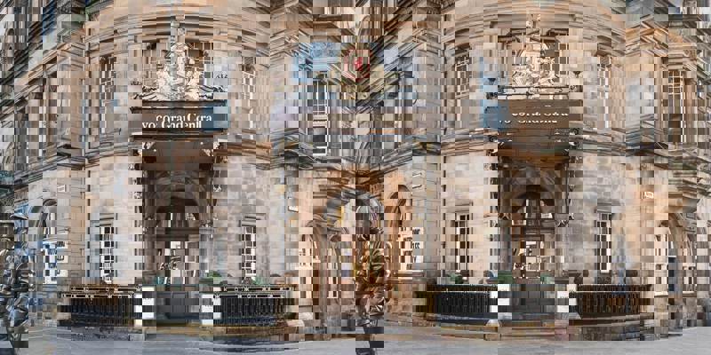 A historic, stone-built hotel in Glasgow, showing a central ornate doorway with a royal crest and a statue of a helmeted figure.