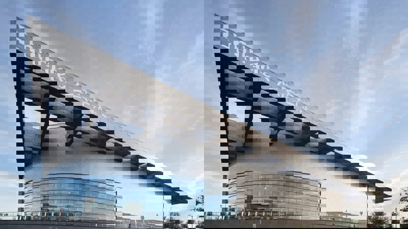 The modern, angular exterior of Emirates Arena with a large glass facade, set against a blue sky.