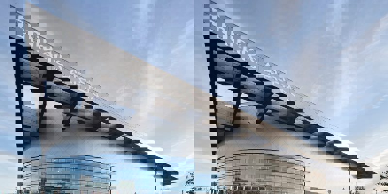 The modern, angular exterior of Emirates Arena with a large glass facade, set against a blue sky.