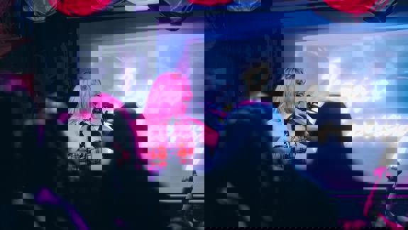 A person with pink hair and a plaid top sings into a microphone on a stage.