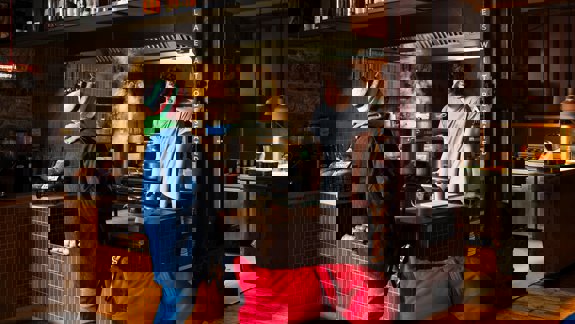 Interior of Outlier cafe with a chef and customer at the counter and an open kitchen. The place is dark and cosy in design.