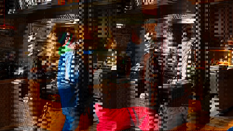 Interior of Outlier cafe with a chef and customer at the counter and an open kitchen. The place is dark and cosy in design.