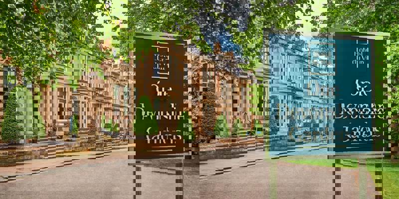 Exterior of One Devonshire Gardens by Hotel du Vin in Glasgow’s West End, showing elegant sandstone townhouses framed by manicured greenery and signage at the entrance.