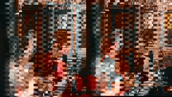 Two people sit at a traditionally decorated bar in conversation with each other, with rustic, exposed stone walls behind them.