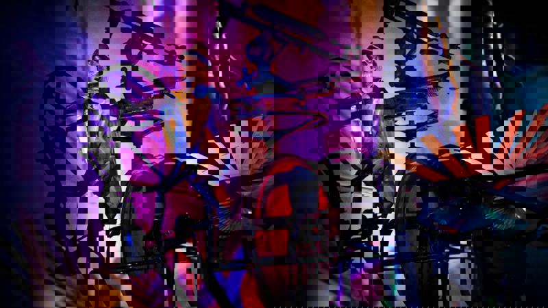 A miniature metal sculpture of a person on a bike with an oversized wheel. Purple and blue lighting shines across the scene.