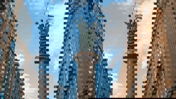 A tall, stone column topped with a metallic, cylindrical sculpture resembling a bouquet of pipes and industrial tools.