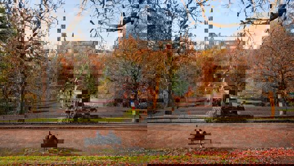 View of Kelvingrove Park in Glasgow during autumn, with people walking across the park bridge and the University of Glasgow tower visible in the background.