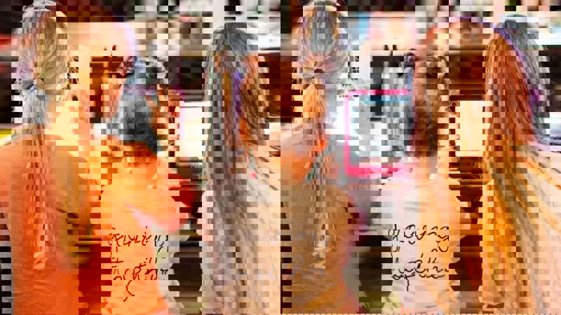 Three children sitting on a bench using electronic devices, with one wearing a shirt that says "growing together".