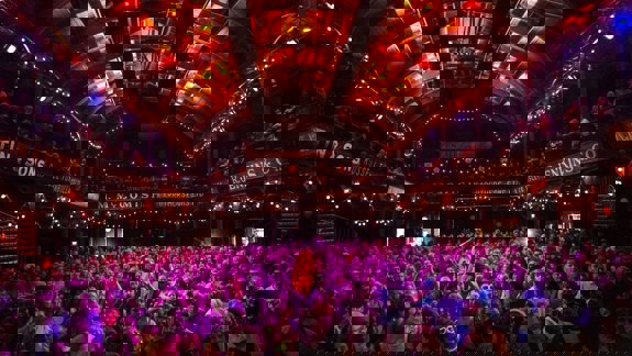 A concert venue with a large, excited crowd and a stage lit with bright magenta lights.