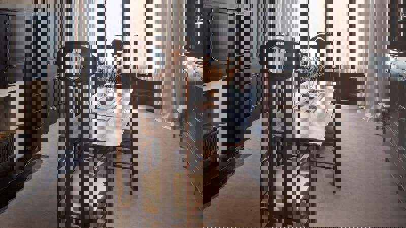 A dining room with dark wood furniture, including a table and chairs, and large bay windows with white curtains.