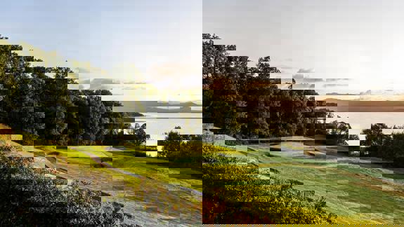 Scenic view of The Carrick golf course at Loch Lomond with bunkers, lush green fairways, and the loch in the loch in the background at sunset.