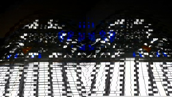 A stained glass window with blue and white panes, and some sections of yellow and clear glass, creating an intricate pattern.