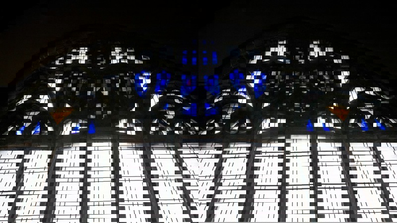 A stained glass window with blue and white panes, and some sections of yellow and clear glass, creating an intricate pattern.