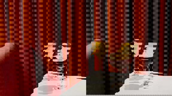 Three different cocktails are on a white table, set against a luxurious terracotta velvet curtain and a pink velour seat.