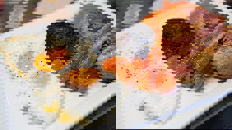 A plate with a full 'English' breakfast including two fried eggs, bacon, sausage, roasted tomatoes, and a mushroom.