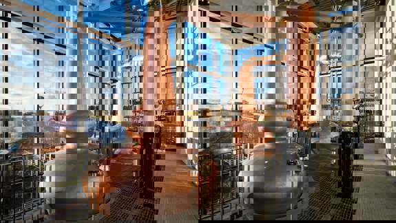 Two large copper whisky stills stand in a room with floor-to-ceiling windows overlooking the River Clyde.