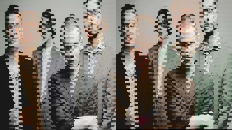 A close-up of four men in suits posing for a photo against a grey background.