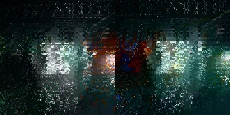 A crowd at SWG3 dances in front of a stage with a bright, abstract digital screen and surrounded by trees.