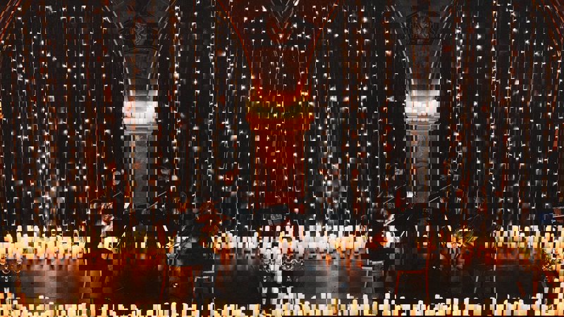 A string quartet performs surrounded by candles and fairy lights in Òran Mór, a former church venue with arched stone details.