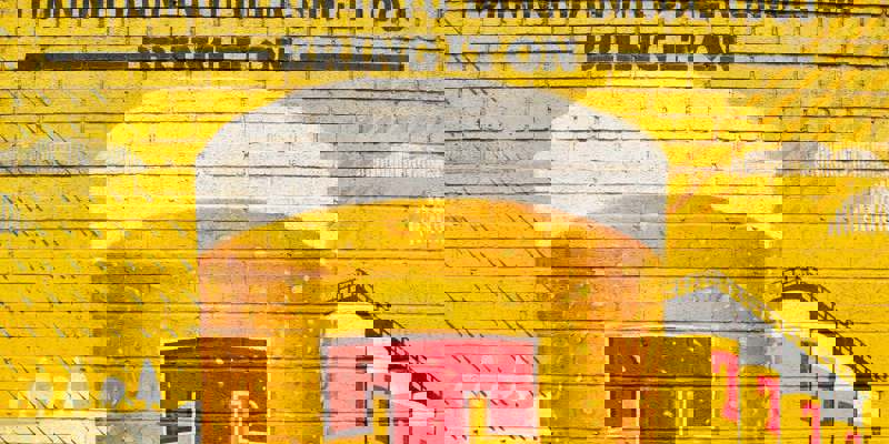 A vibrant yellow brick wall mural depicting a large beer glass with "Tennent's" and "Turning Rain into Beer Since 1885".