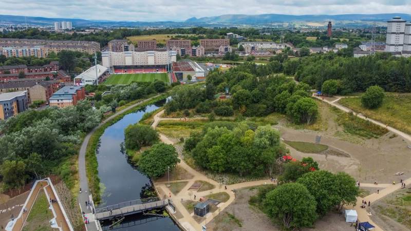 Aerial view of the Glasgow to Edinburgh canal route with footpaths, greenery, and the city skyline in the background.