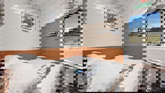 A clean, modern double berth cabin on the Caledonian Sleeper train with a made-up bed, a small sink area, and a window showing a Scottish countryside view.