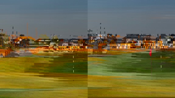 Fairway at Prestwick Golf Club leading to the traditional clubhouse, bathed in golden evening light.