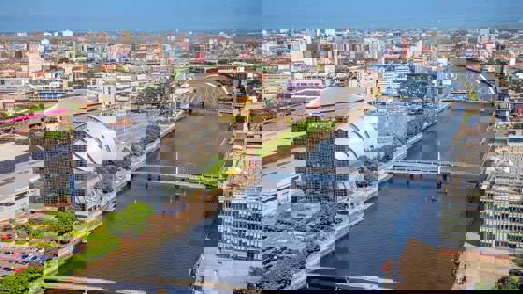 An aerial view of the River Clyde winding through Glasgow, with modern buildings and several bridges spanning the water.