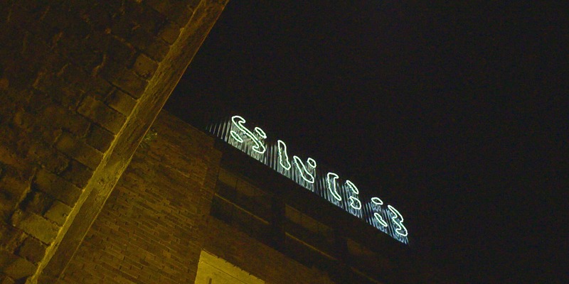 A neon sign for "SWG3" glows on the top of a brick building at night.