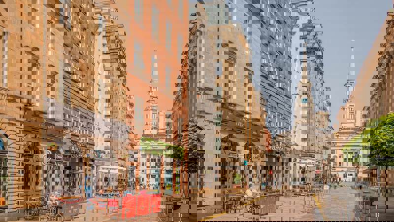 A street scene of stone buildings with shops and restaurants in Glasgow's Merchant City area.