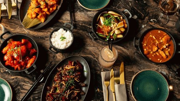 Overhead view of a variety of colourful Asian dishes, including rice, stir-fry, and curry, served on a dark marble table
