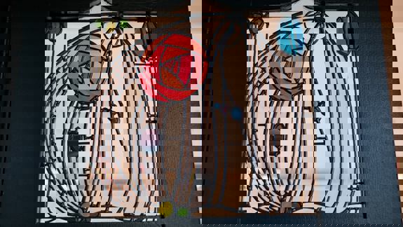 A close-up of a vibrant stained-glass panel with a stylized red rose, set into a dark wooden frame.