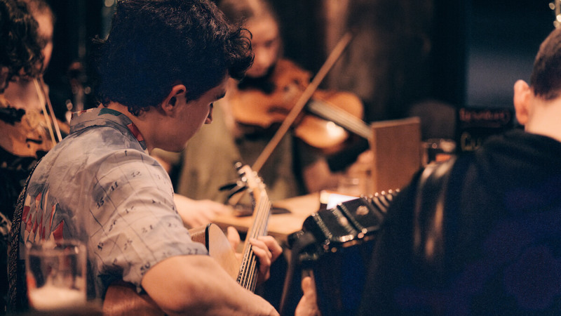 A group of young musicians plays traditional instruments in a cosy pub