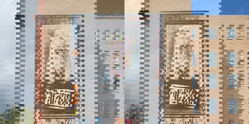 Mural of comedian Billy Connolly as an older man with long white hair and glasses, on a brick building.