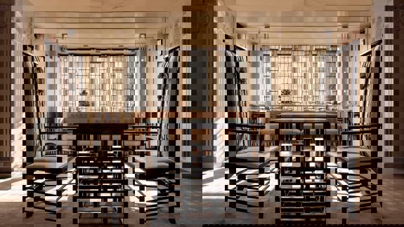 A brightly lit interior with two tall, dark chairs facing a low table, all in a distinctive Art Nouveau style.