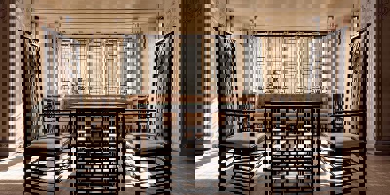 A brightly lit interior with two tall, dark chairs facing a low table, all in a distinctive Art Nouveau style.