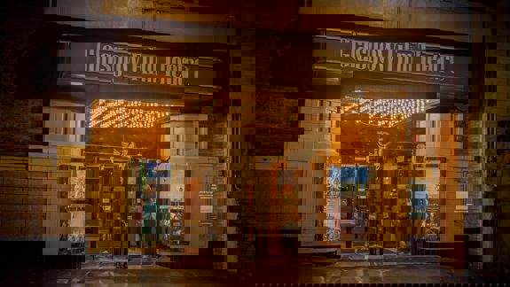 Glasgow Film Theatre exterior at night, with a person entering under a brightly lit marquee displaying movie posters.