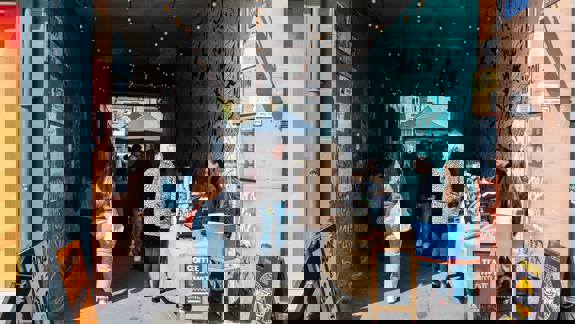 A busy outdoor market in an alleyway with stalls and people walking around. 