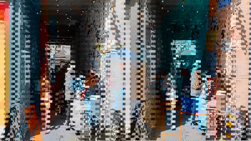 A busy outdoor market in an alleyway with stalls and people walking around. 