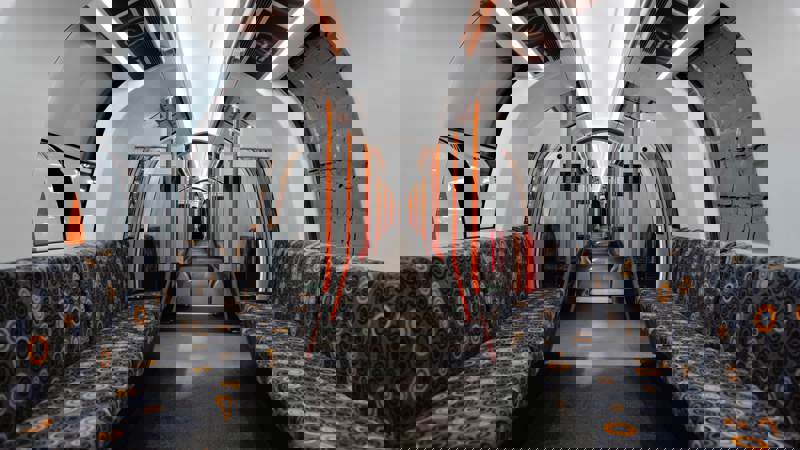 The interior of a modern, empty subway train features patterned seats, bright lighting, and sleek orange handrails.