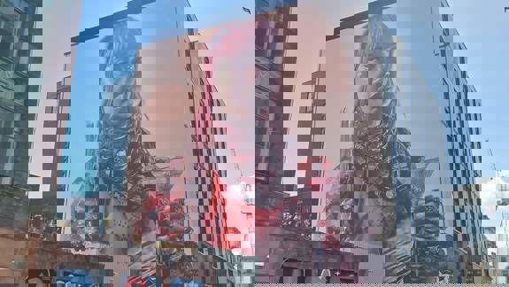 A striking mural of a woman with pink hair, holding a lit candle and a martini glass. The mural covers the side of a large building, The Social Hub, with smaller street art visible below.