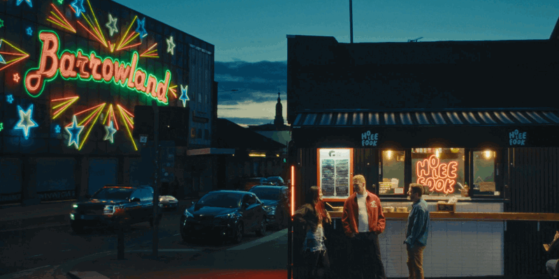 Neon-lit night scene: Barrowland sign with stars, a takeaway shop (Ho Lee Fook) on the right, and three people talking outside in Glasgow, Scotland.