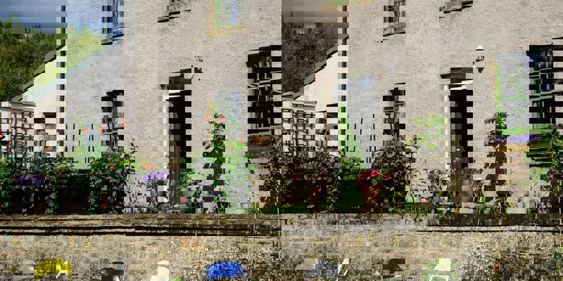 A simple, stone building with bright green windows and a garden with raised planters. A few folding chairs are on the lawn.