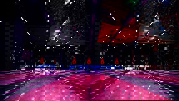 A view down a bowling alley with pink glowing lanes and pins at the end.